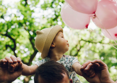 little girl sitting on her father's shoulders looking at pink balloons