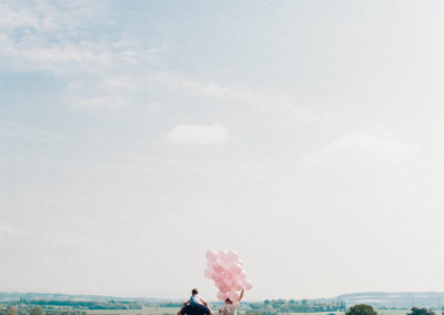 family in a field holding a big bunch of pink balloons