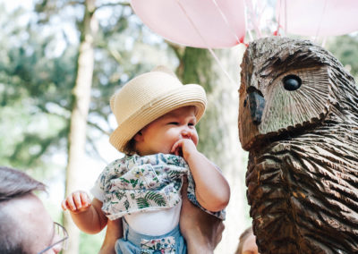baby girl being held up next to wooden sculpture in the woods
